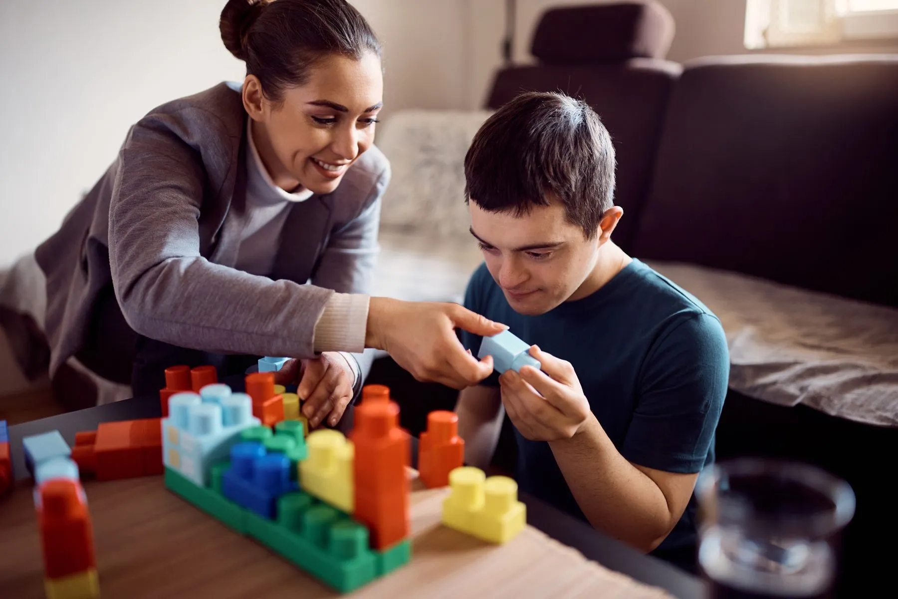 Attending Care direct support professional helping a young man build with colorful blocks
